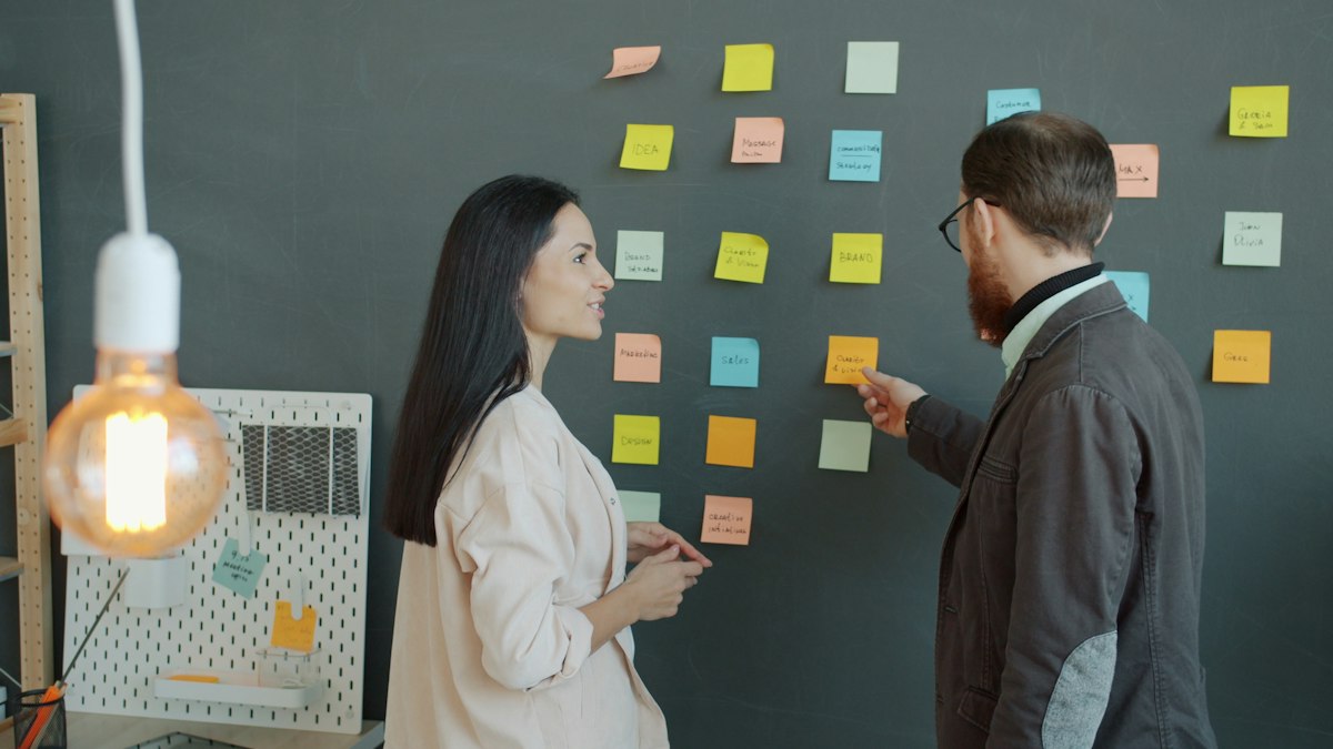 Two colleagues mapping steps on a wall of sticky notes to define a repeatable process