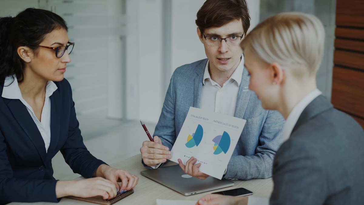 Three colleagues in a meeting reviewing sales charts to decide which accounts to pursue